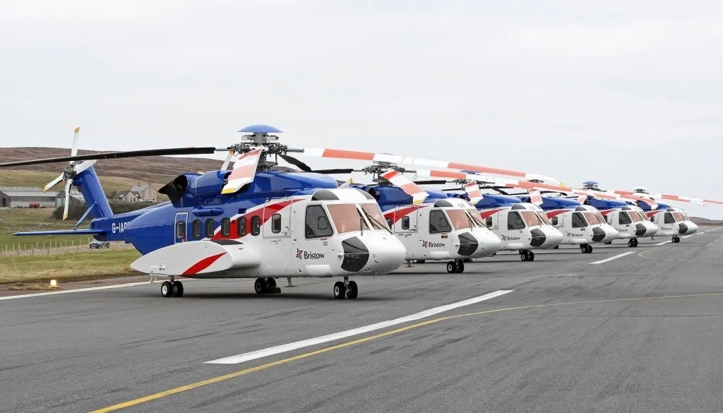 Rekke med parkerte redningshelikoptre på en flyplass.